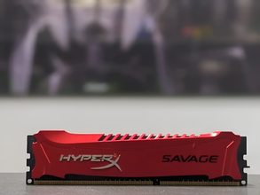 Red HyperX Savage RAM module on a blurred gaming setup background