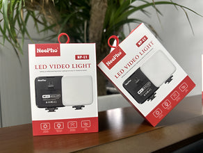 Two NeePro LED video lights in their packaging on a wooden surface with a plant in the background.