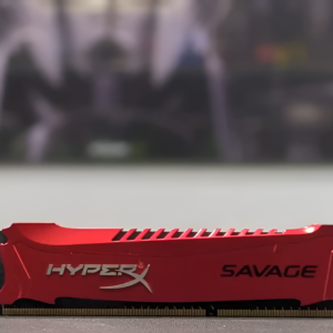 Red HyperX Savage RAM module on a blurred gaming setup background