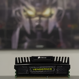 Corsair Vengeance RAM module on a desk with a blurred background featuring a character with glowing eyes.